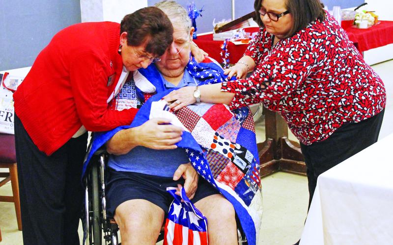 Quilts of Valor volunteer Stamie Cline (left) embraces United States Air Force veteran and Brian Center resident Ephraim “E.K.” Brown as Brian Center Administrator Shelley Tinsley helps wrap Brown in his Quilt of Valor. Brown, 67, is a highly decorated veteran who served more than 20 years in the Air Force, including three tours of duty in Germany. (Cory Spiers/MNJ)