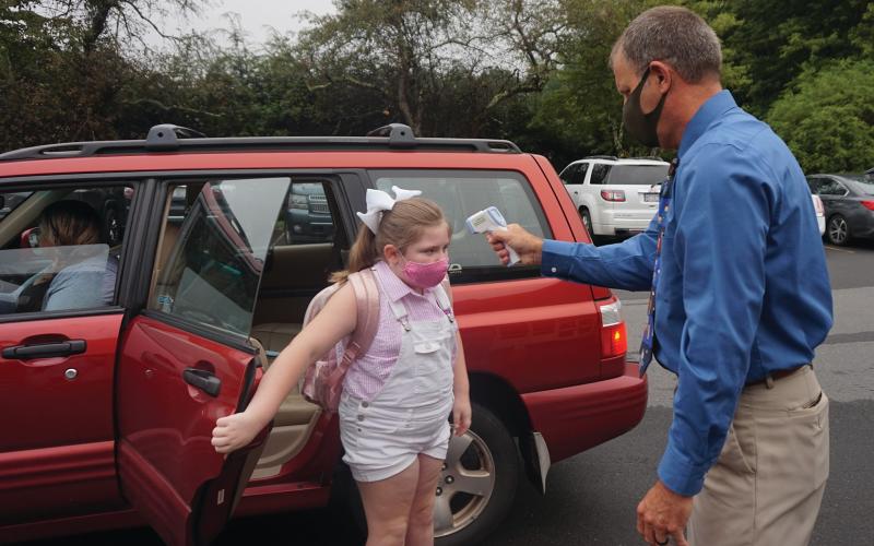 Gouge Elementary School Principal Colby Calhoun uses an infrared thermometer to take the temperature of third grader Holland Atkins on the first day of school Monday, Aug.17. Temperature checks are required and masks were provided for all. (Photo by Stephanie Chang Pitman)