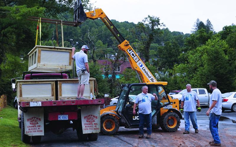 Volunteers from The Quartz Corp. confer as they prepare to use heavy equipment to lift a garden bed off of a truck. The volunteers, as part of Quartz Corp.’s annual Volunteer Impact day, built and placed 16 raised beds for the new community garden in Spruce Pine Riverside Park. (Photo by Stephanie Chang Pitman)