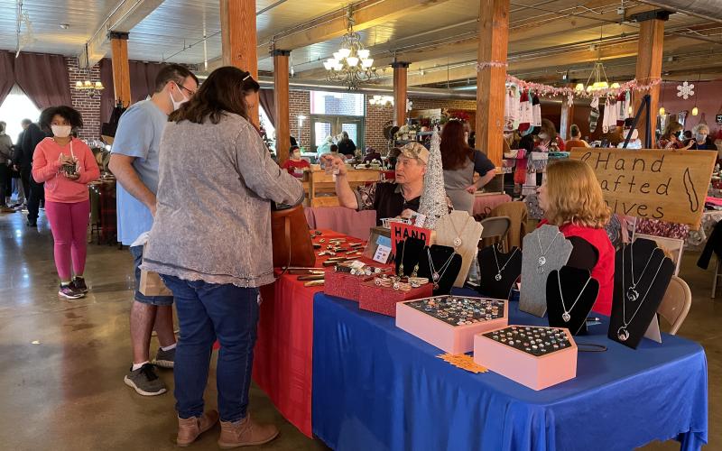 (Top): Visitors to the Spruce Pine Southern Christmas Show browse the wares of one of the 40 vendors that set up on Saturday, Nov. 28 at the show at the Cross Street Commerce Center. (Bottom): Vendors at the Spruce Pine Southern Christmas Show sold a myriad of goods ranging from homemade holiday items to tupperware and plenty in between. (MNJ photos/Juliana Walker)