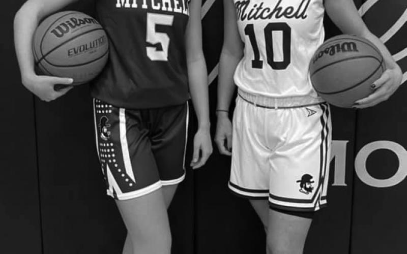 Mitchell High School junior Chandra Jenkins (left) and senior Marley Cloer (right) pose in the school gym to show off the new uniforms for the girls’ basketball team. The new purple jersey features block lettering on the front and the new white jersey features cursive lettering. The team, which is coming off of a 22-6 campaign, will start official organized practices this month and will begin a shortened season in January. (Submitted photo)