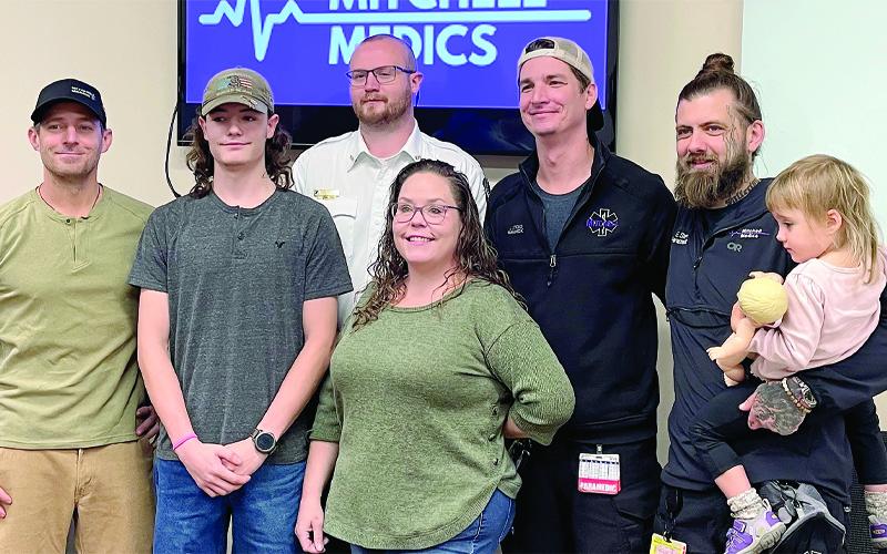 MNJ Photo/Mariel Williams.  Mitchell Medics honored four employees recently for their efforts to save a teenager in a medical crisis the morning Hurricane Helene knocked out communications in Mitchell County. From left are Dr. Gabriel Cade of Blue Ridge Regional Medical Center, patient Devon Hughes, and Mitchell Medics staffers Alex Brown, Jared Stickle and Evan Stern, holding Millicent Stern.
