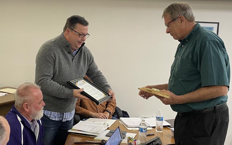 MNJ Photo/Mariel Williams.  Mitchell County Commissioner Steve Pitman, standing left, presents John Boyd with a plaque honoring him for his service. Boyd retired as president of Mayland Community College Friday.