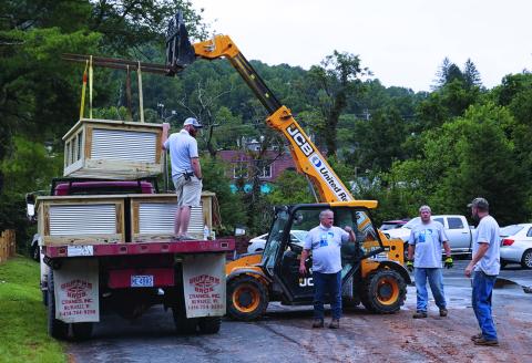 Volunteers from The Quartz Corp. confer as they prepare to use heavy equipment to lift a garden bed off of a truck. The volunteers, as part of Quartz Corp.’s annual Volunteer Impact day, built and placed 16 raised beds for the new community garden in Spruce Pine Riverside Park. (Photo by Stephanie Chang Pitman)