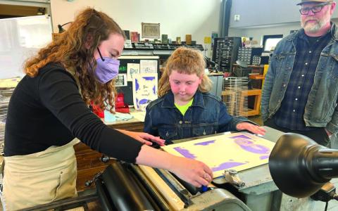 MNJ Photos/Noreen Nickolas.   Volunteer Roby Summerfield, on left, shows Sonny Smith how to make a poster with a letterpress, while his father, Eric Smith watches.