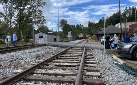 MNJ Photo/Mariel Williams.  A small crowd gathered on Lower Street (Locust Avenue) to see the first freight train pass through Spruce Pine since Hurricane Helene. The train was pulled by a commemorative engine labeled with the old Clinchfield logo.