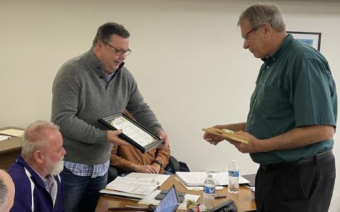 MNJ Photo/Mariel Williams.  Mitchell County Commissioner Steve Pitman, standing left, presents John Boyd with a plaque honoring him for his service. Boyd retired as president of Mayland Community College Friday.